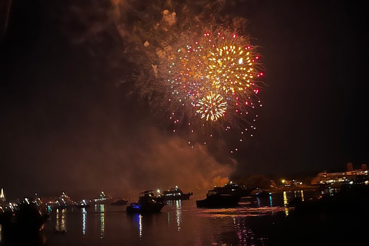 Bright fireworks over water with boats in the foreground at night.