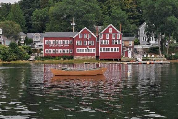 Red boat shop by a lake with a brown boat in the foreground and green trees in the background.