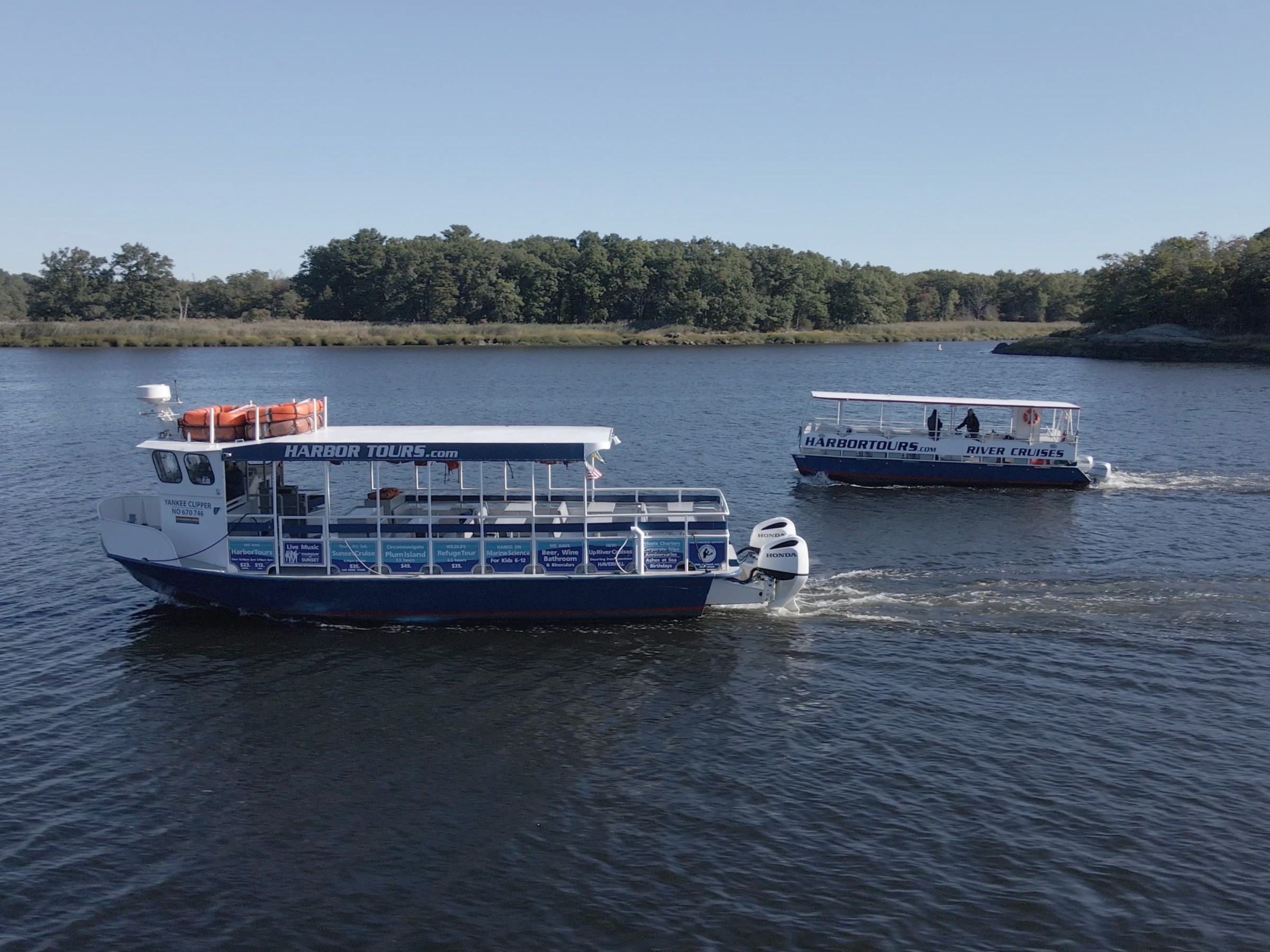 Two tour boats cruising on a wide river with trees in the background.