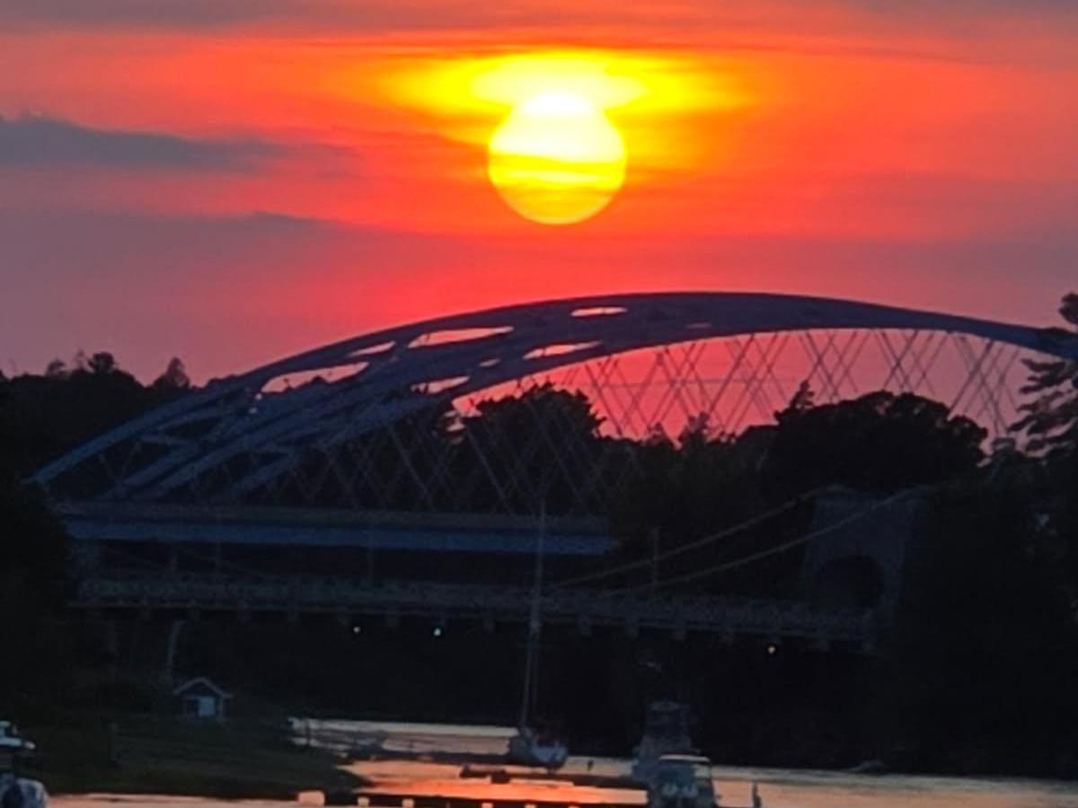 Sunset over a bridge with a vibrant orange and pink sky reflecting on the water.