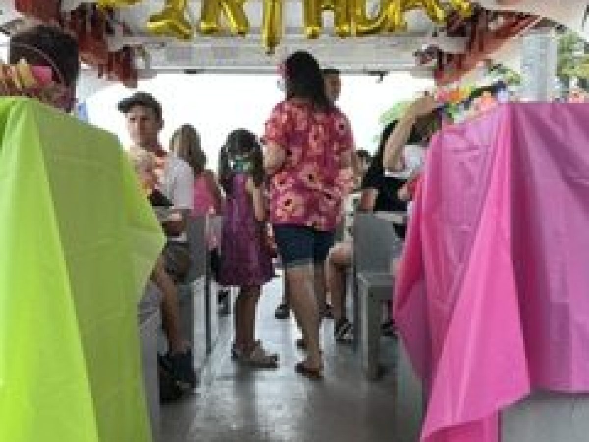 People on a boat celebrating a birthday with colorful tablecloths and balloon letters.
