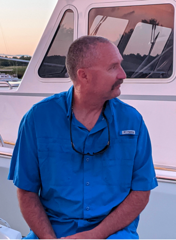 Man in blue shirt sitting on a boat, looking sideways during sunset.