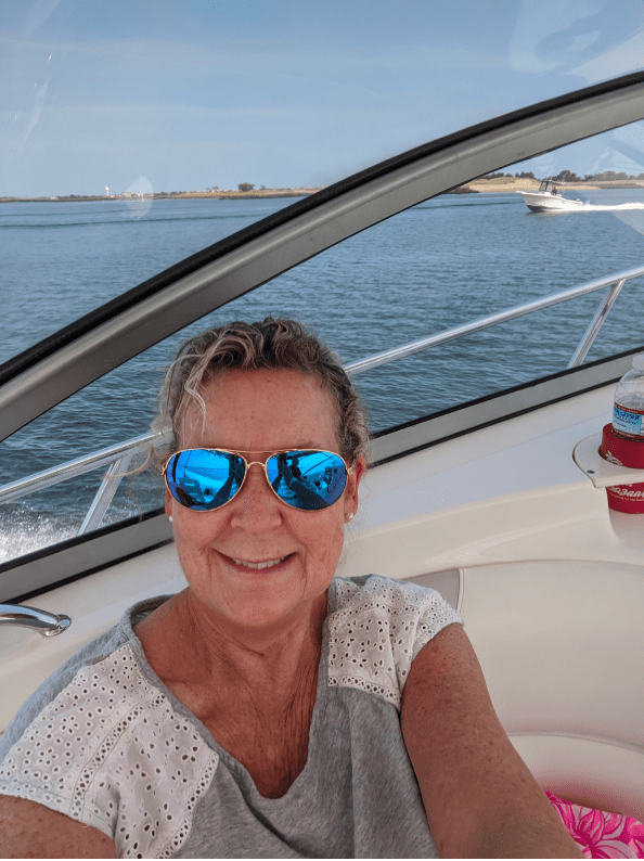Person in sunglasses smiling on a boat with water and another boat in the background.