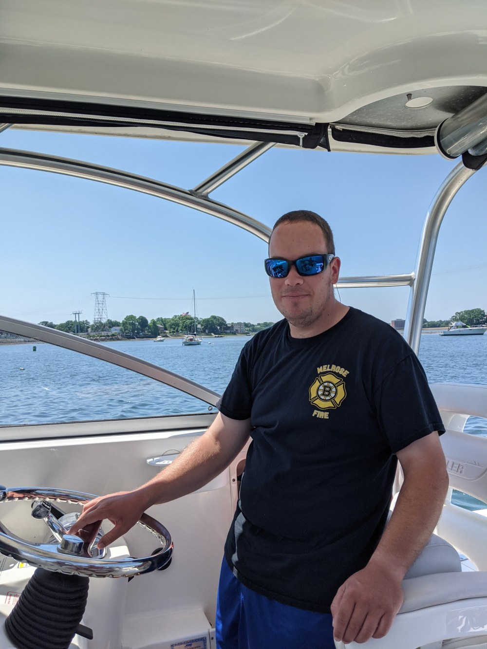 Man in sunglasses steering a boat on a sunny day.
