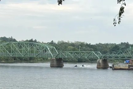Green truss bridge over a river with trees in the background.